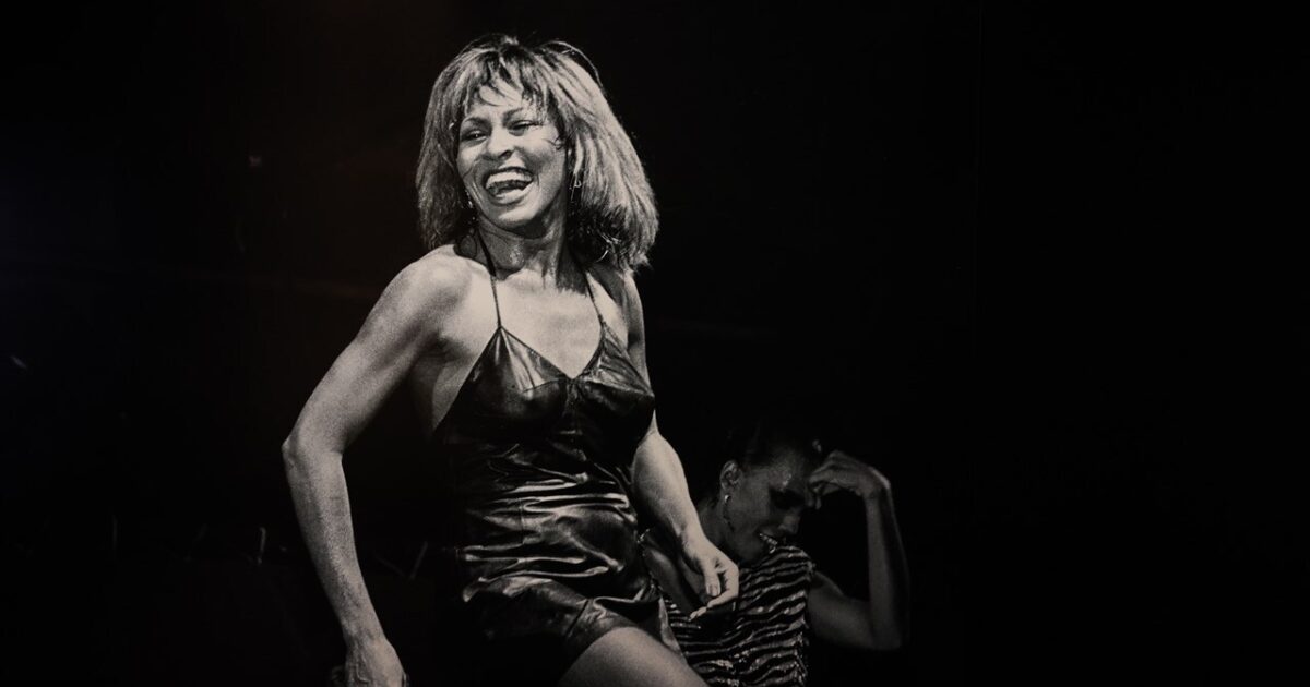 Zwart wit foto van een dansende en lachende Tina Turner